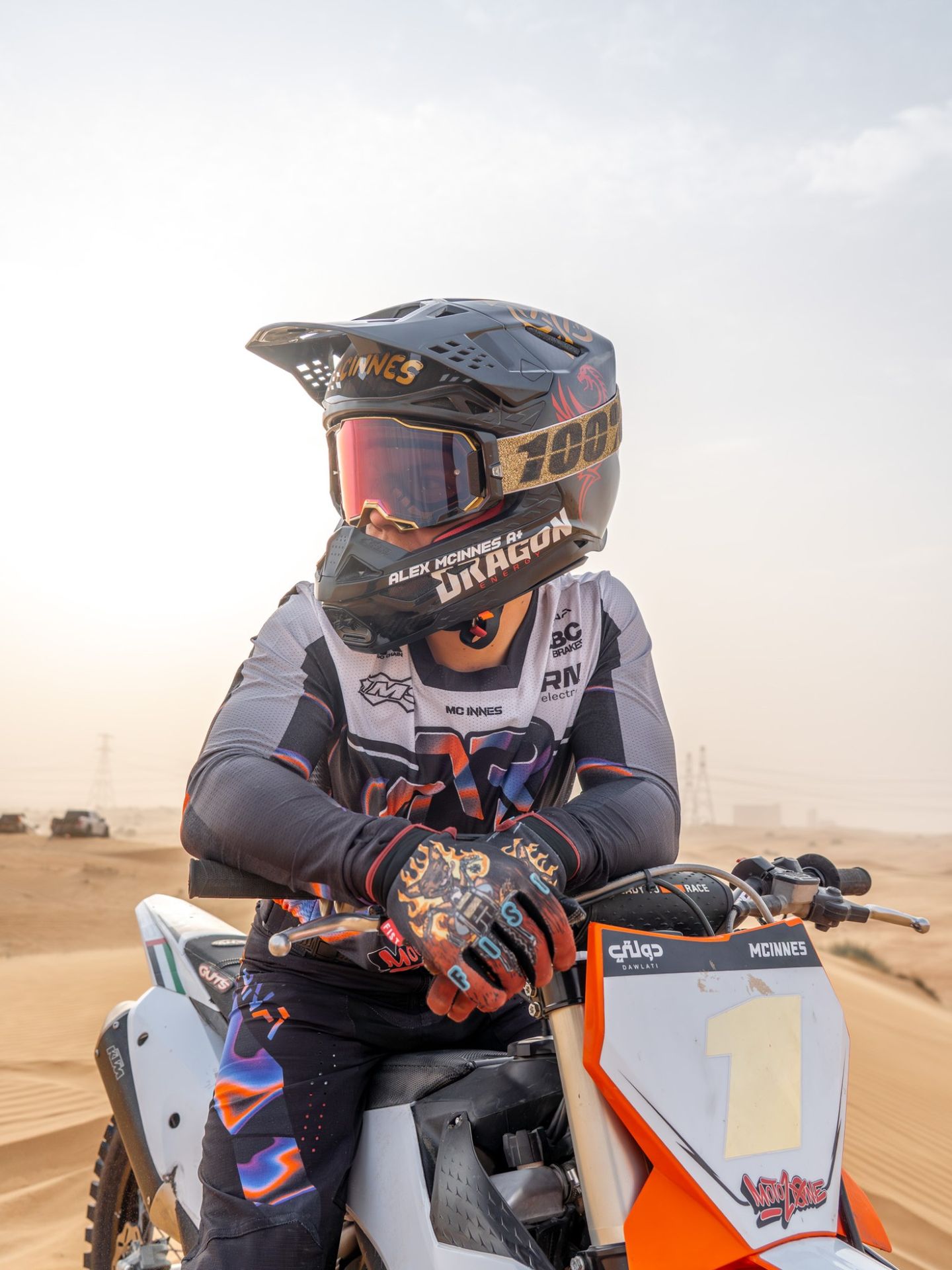 Alex McInnes in his helmet and goggles, leaning on the handlebars of his bike in the dunes
