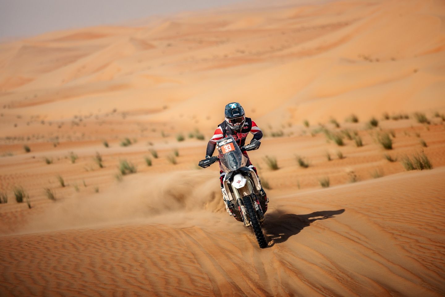 Alex McInnes racing down a dune towards the camera, sand spraying from the rear wheel